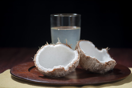 Fresh young coconut in broken shell with glass of coconut water on platter with black backgroundの写真素材
