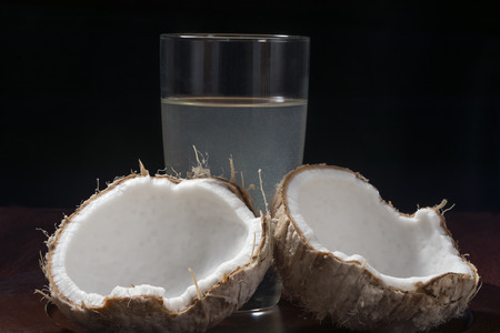 Fresh young coconut in broken shell with glass of coconut water on platter with black backgroundの写真素材