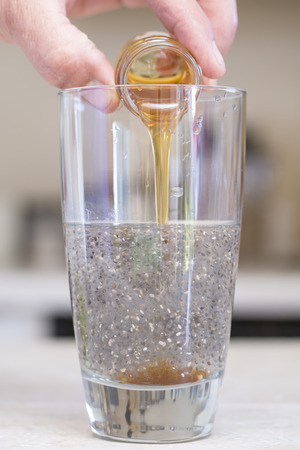 Closeup of hand pouring small jar of honey into clear glass beverage of water and chia seedsの写真素材