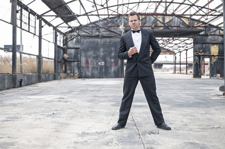 Formal dressed tough Caucasian man stands ready in action pose in burned down warehouseの写真素材