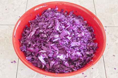 Big red ceramic bowl filled with chopped purple cabbage on tile counterの写真素材