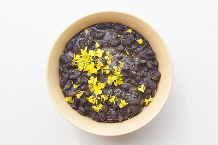 Top view of bowl of cooked black turtle beans with yellow mustard flowers sprinkled on topの写真素材
