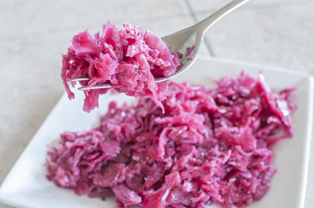 Closeup of fork full of fresh homemade sauerkraut with plate in background on tile counterの写真素材