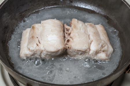 Closeup of fillet of mahi-mahi fish fillet cooking in water and oil in skillet on stoveの写真素材