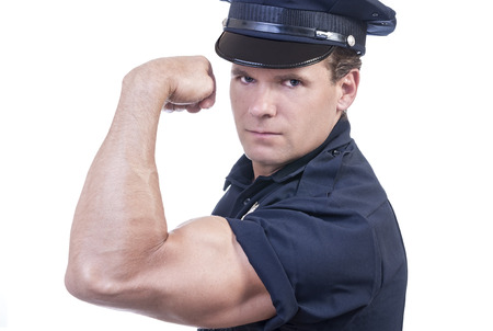 Male police officer in blue uniform flexes arm to show power of the law on white backgroundの写真素材