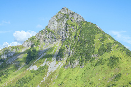 Rocky rugged Arrowhead Peak near Sitka, Alaska with green forested slopes on clear sunny day with blue skyの写真素材