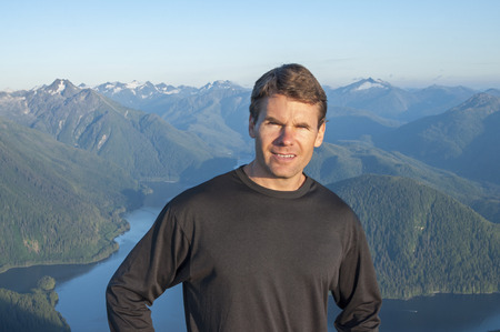 Caucasian male hiker in black shirt stands on top of mountain with beautiful scenic view of bay and mountains of Baranof Island in Alaskaの写真素材