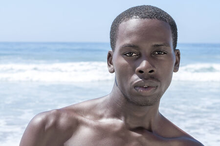 Closeup portrait of sexy and handsome young African American man shirtless on sunny beach in summerの写真素材