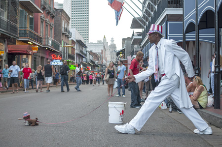 NEW ORLEANS, USA - OCTOBER 10, 2014: Man dressed in white suit and patriotic hat stands frozen in stride on Bourbon Street as if walking a small stuffed dog.のeditorial素材