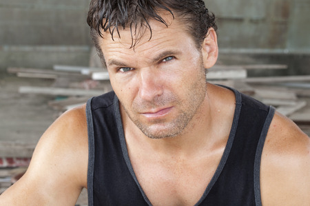 Closeup portrait of unshaven sweaty Caucasian man in black tank top working in construction areaの写真素材