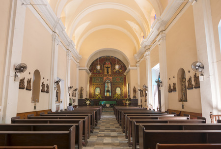 Interior of Cathedral of San Juan Bautista in Old San Juan, Puerto Rico showing altar and wooden pews with one faithful worshiperのeditorial素材