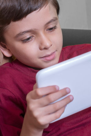 Handsome young boy in red shirt enjoys playing his tabletの写真素材