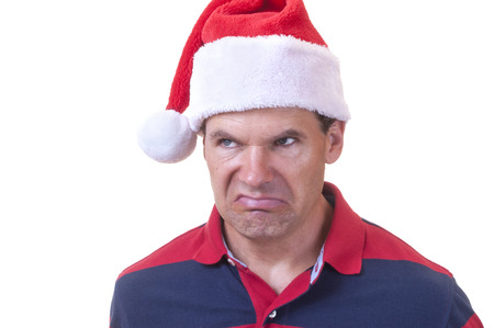 Portrait of grumpy Caucasian man wearing casual shirt and red Santa hat making ugly grinch face on white backgroundの写真素材