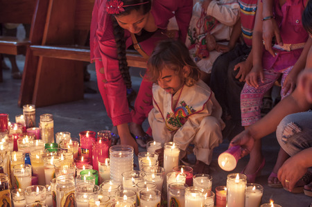 LAS CHOAPAS, MEXICO - DECEMBER 12, 2014: A young boy dressed traditionally as Juan Diego is helped by his mother as he places a candle among many others on a church floor after a mass celebrating the Feast of Our Lady of Guadalupeのeditorial素材