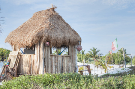 Palm-thatched hut with stick walls and hammocks inside on white sand beach in Tulum, Mexicoの写真素材