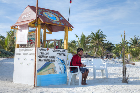 TULUM, MEXICO - JANUARY 23, 2015: A local fisherman sits at a kiosk on a white sand beach offering fishing tours to catch local gamefish in Tulum, Mexicoのeditorial素材