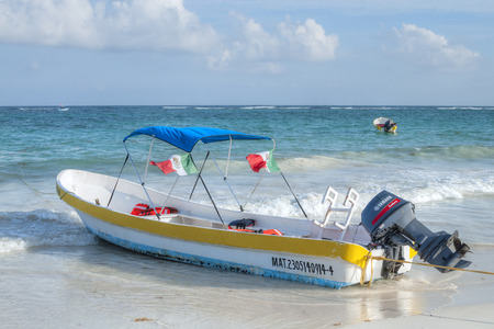 TULUM, MEXICO - JANUARY 23, 2015: A local panga boat used for fishing or other recreational purposes sits anchored in shallow waves on beach in Tulum, Mexicoのeditorial素材