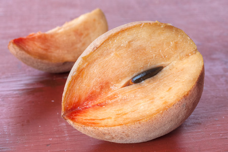 Closeup of ripe cut sapodilla chicozapote fruit and slice on red tableの写真素材