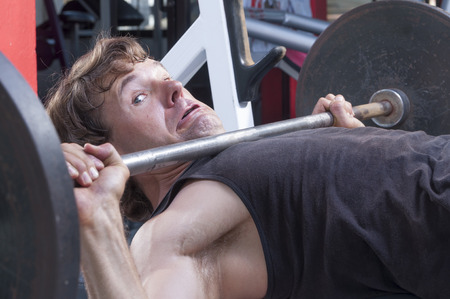 Caucasian man working out in gym is stuck under heavy barbell on bench pressの写真素材