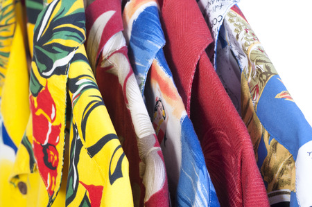 Closeup selection of five colorful yellow, red, blue and green Hawaiian shirts arranged on hangers on white backgroundの写真素材