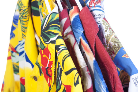 Selection of five colorful yellow, red, blue and green Hawaiian shirts arranged on hangers on white backgroundの写真素材