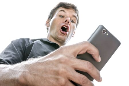 Low angle closeup Caucasian man looking down at his cell phone shows expression of shock as he opens his mouth in disbelief on white backgroundの写真素材