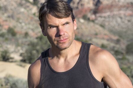 Closeup head shot of bold adventurous Caucasian man with serious expression gazing in bright sunlight in the distant desertの写真素材