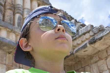 Low angle closeup of young tourist wearing high reflective sunglasses showing majestic Maya pyramid at archaeological site of Uxmal, Yucatan, Mexicoの写真素材