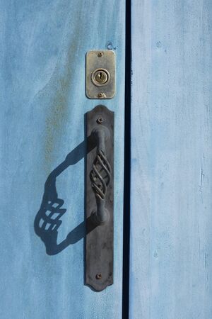 Closeup and shadow of black iron door handle and brass key lock on exterior of blue wooden door in Valladolid, Mexicoの写真素材