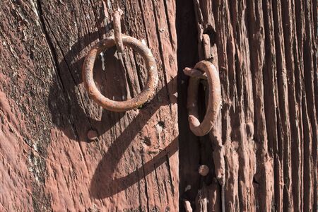 Closeup and shadows of rusty red rings on weathered wood door with peeling paint in Valladolid, Mexicoの写真素材