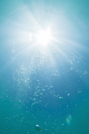 Low angle shot underwater looking up at sun as rays diffuse through water and bubbles float up toward surfaceの写真素材