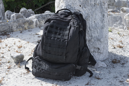 Black military backpack leaning against stone column at Maya archaeological site of El Rey in Cancun, Mexicoの写真素材