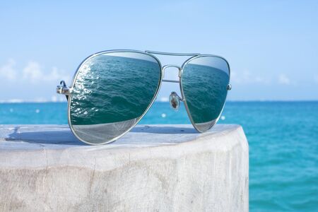 Closeup of reflective sunglasses on wooden post of dock reflecting image of beautiful blue sea on sunny dayの写真素材
