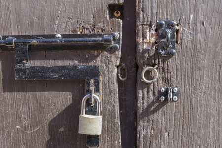 Closeup of key padlock and unlocked metal rings on rustic weathered wooden door in natural exterior lightingの写真素材