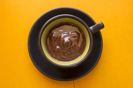 Closeup high angle thick dark chocolate in a cup on a saucer on yellow tableの写真素材