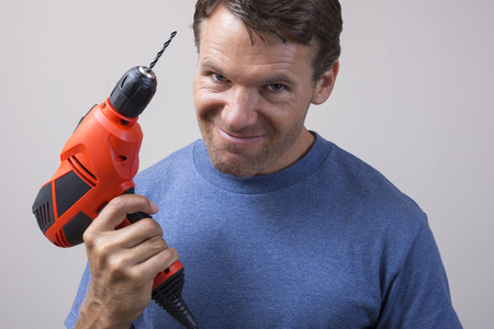 Closeup of handsome Caucasian man holding electric power drill with expression of readiness looking into cameraの写真素材