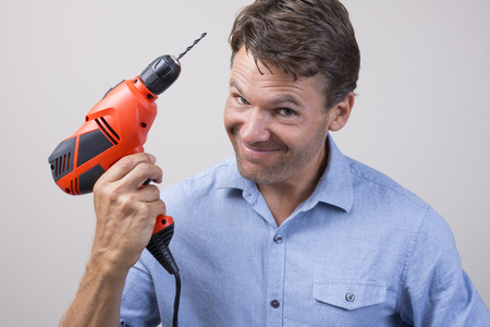 Closeup of handsome Caucasian man holding electric power drill with expression of readiness looking into cameraの写真素材