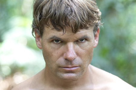 Closeup head shot of sweaty Caucasian man with serious bold expression looking into camera in wilderness surroundingsの写真素材