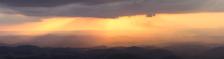 Beautiful scenic hilly landscape panoramic illuminated by brilliant orange afternoon sunlight from behind gray clouds in Minas Gerais, Brazilの写真素材
