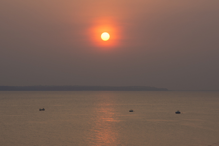 Vermillion sunset penetrates hazy sky while reflecting over calm surface of Rio Negro at Ponta Negra near Manaus, Amazonas, Brazilの写真素材