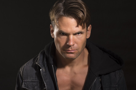 Portrait of handsome sexy Caucasian man with bold eyes and serious expression wearing open jacket revealing pectoral definition on black backgroundの写真素材