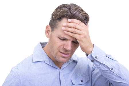Closeup of handsome Caucasian man wearing blue button down shirt and holding hand on head with look of frustration or suffering from painful headache on white backgroundの写真素材