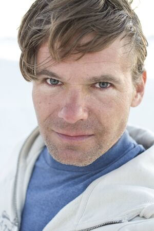 Closeup portrait of handsome Caucasian man with messy brown hair looking at camera on windy day wearing blue shirt and jacket outsideの写真素材