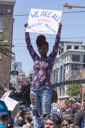 SAN DIEGO, USA - MAY 27, 2016: An Afro American woman holds high a sign reading "We are all women" at an anti-Trump protest outside a Trump rally in San Diego.のeditorial素材