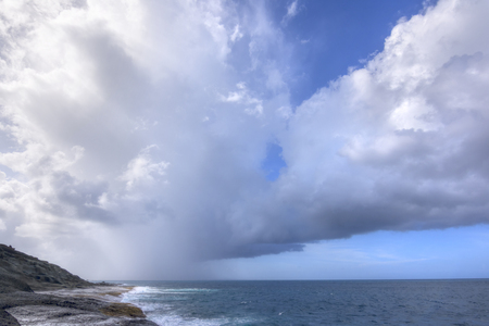 Rain falls from dark clouds out at sea from rocky northeast coast of Isla Culebra in Caribbean Seaの写真素材