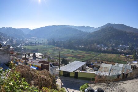 Plots of farmland in valley of San Nicolas bordered by small housing communities in San Cristobal de las Casas, Chiapas on sunny morningの写真素材