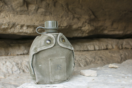 Canvas covered U.S. army canteen sits on rock at entrance to rocky cave in natural lightingの写真素材