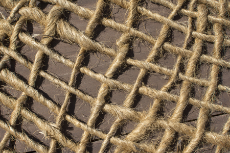 Closeup loosely woven net made of natural rope fibers lying over wood in sun with strong shadowsの写真素材