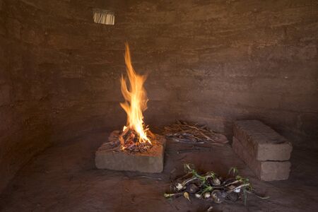 Small campfire burning on bricks inside primitive adobe hut with dirt floor and wild soap plant roots to be roastedの写真素材