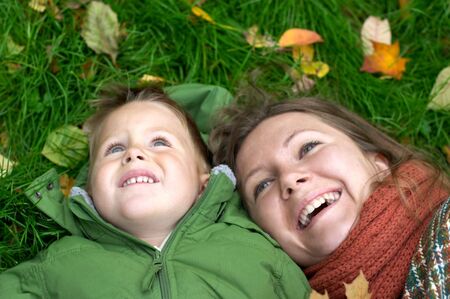 Smiling mother and son on the grass covered with fallen leavesの写真素材